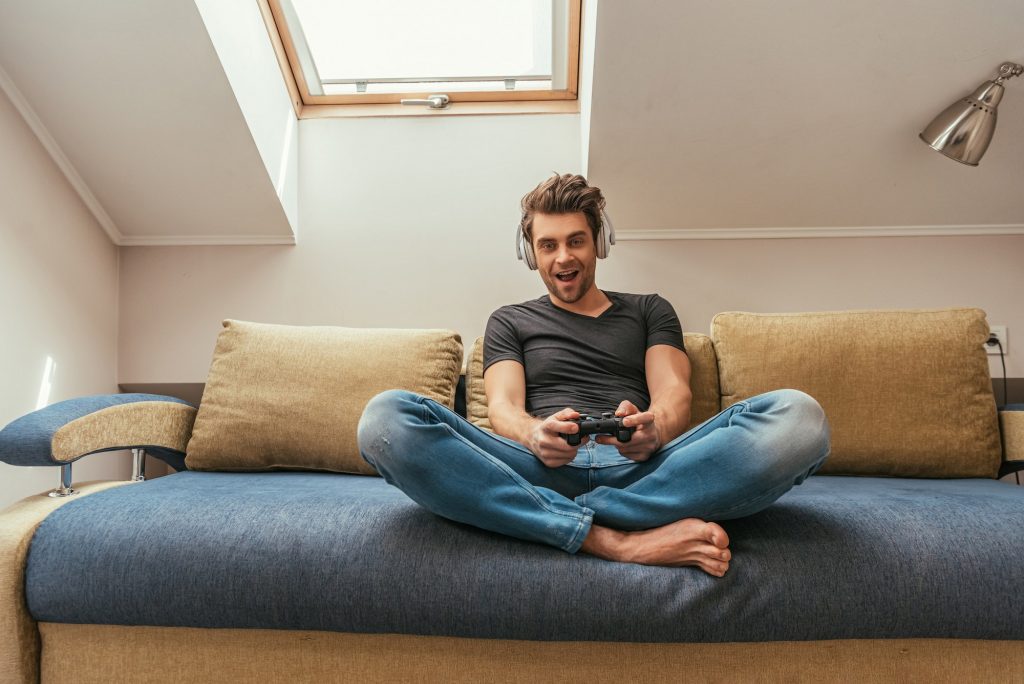 KYIV, UKRAINE - APRIL 13, 2019: excited man in wireless headphones on neck playing video game while